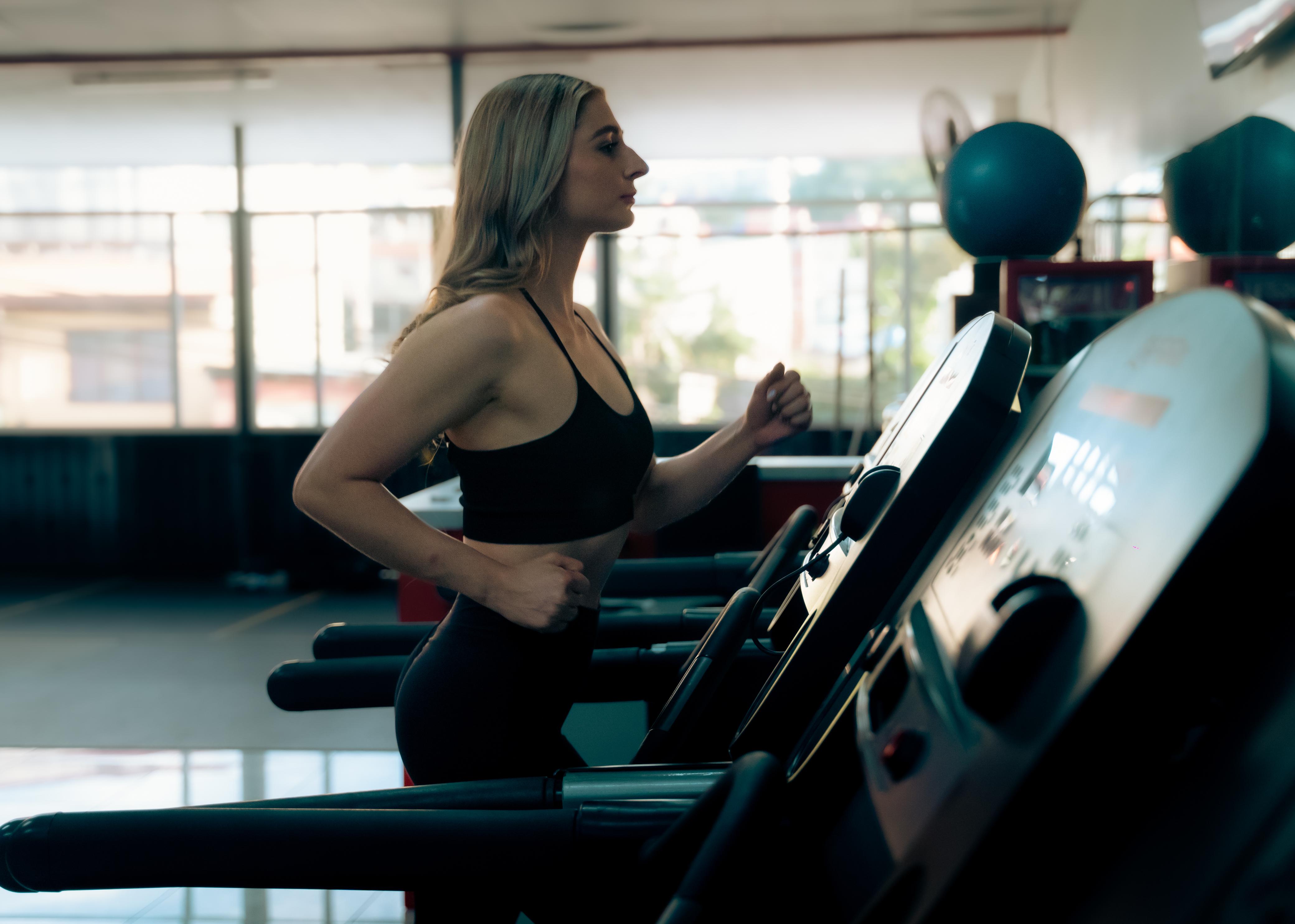 Mujer corriendo en faja en Elite Fitness Club, luz natural desde los ventanales