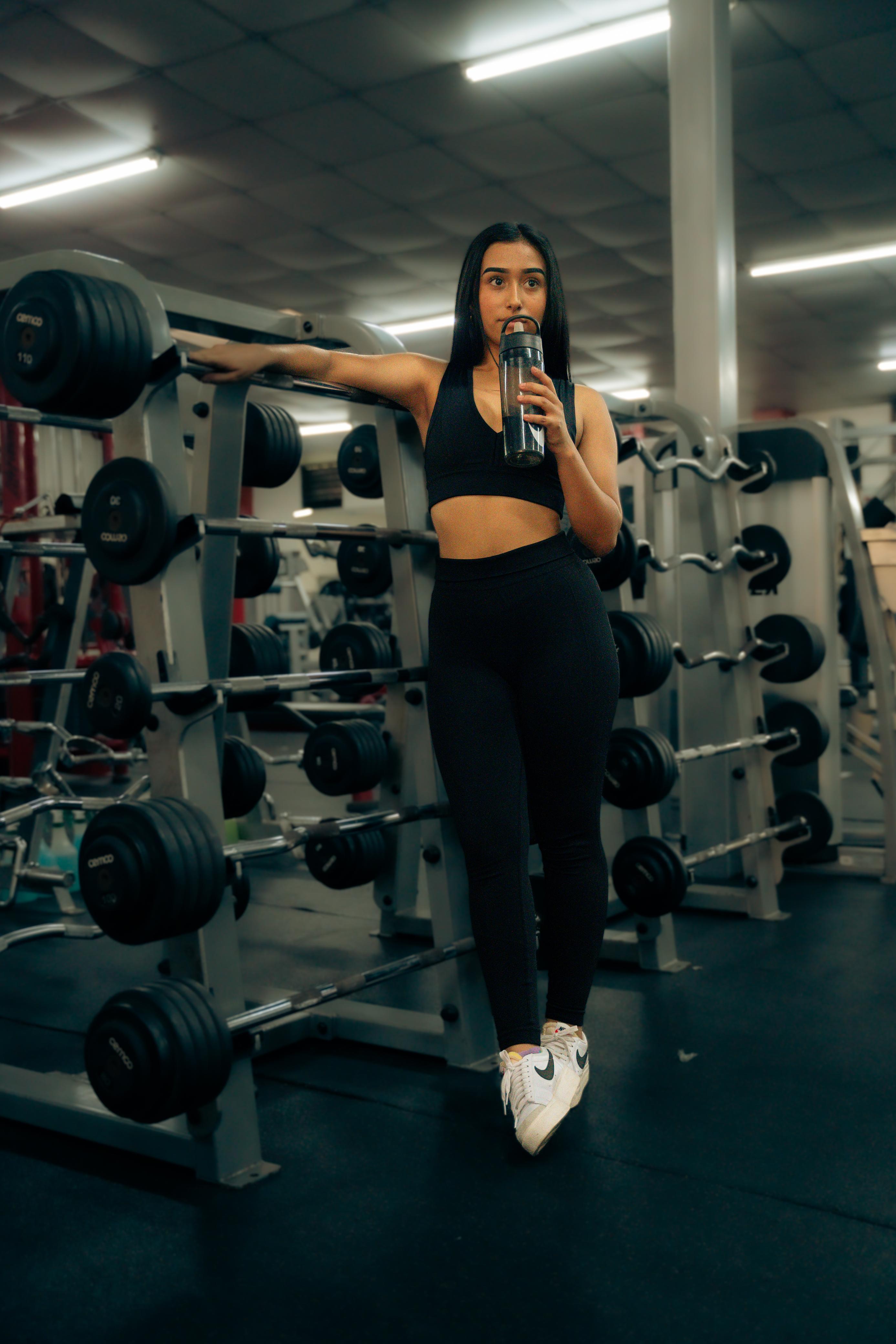 Mujer tomando agua junto al rack de mancuernas en Elite Fitness Club