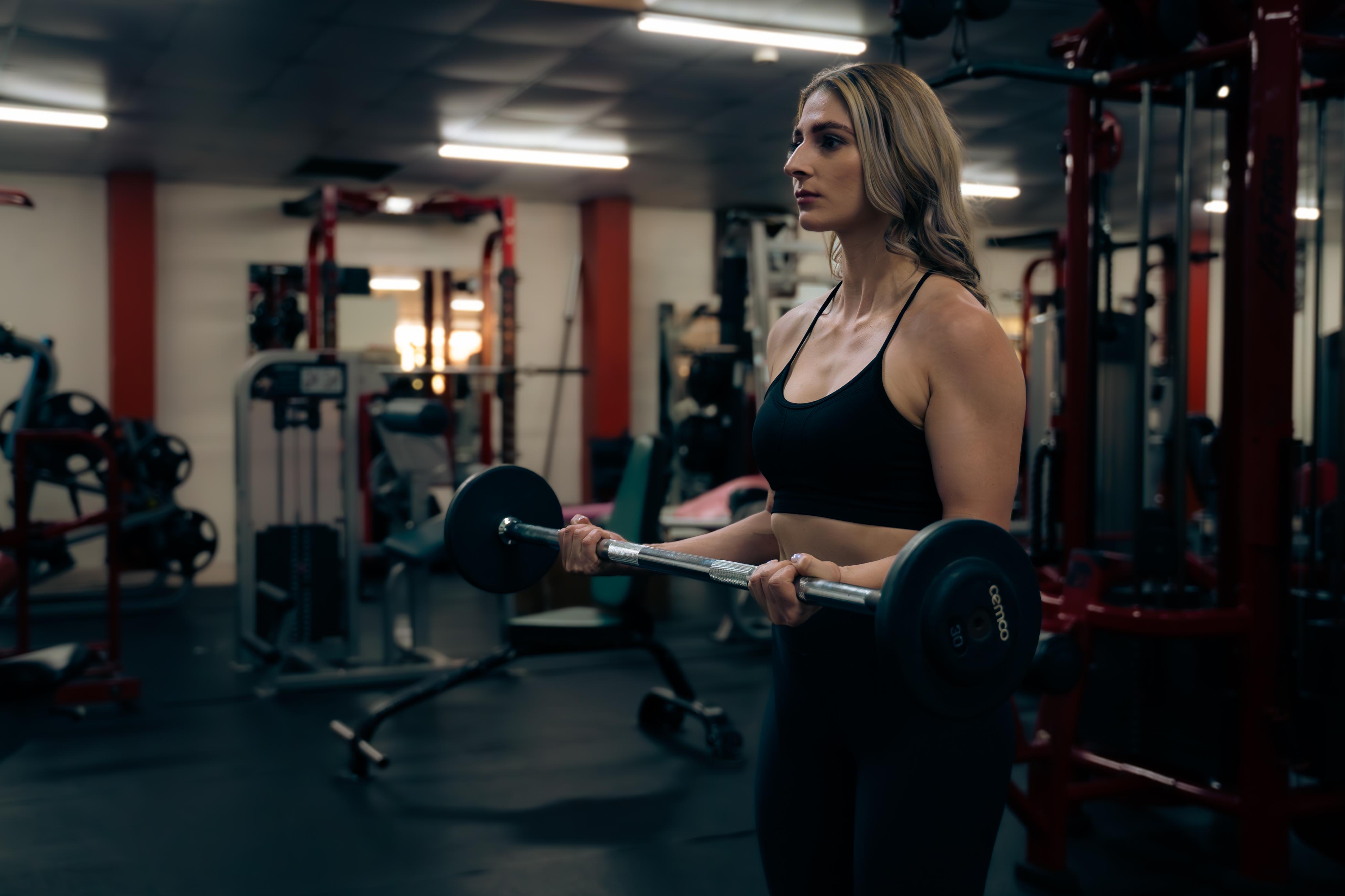 Mujer haciendo curl con barra en Elite Fitness Club